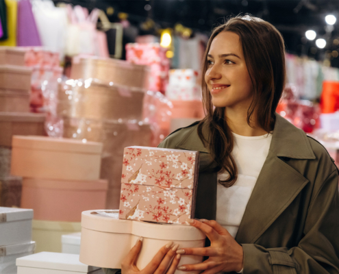 Smiling Woman Holding Floral Wrapped Gift Boxes While Shopping Among Colorful Displays